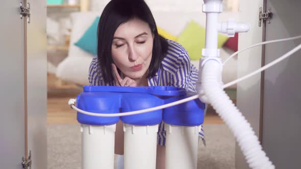 Young Woman Housewife Looks Under the Sink and Examines the Water Filter