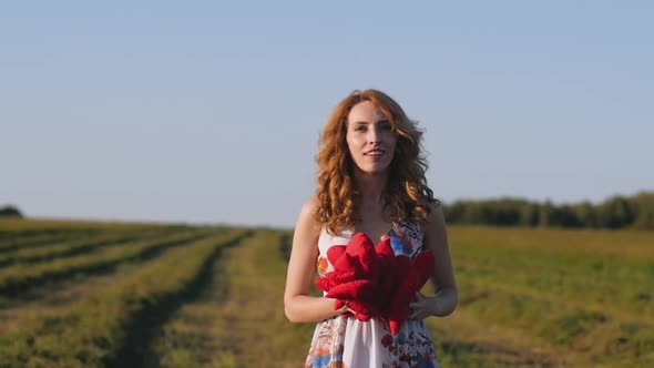 Redhead Young Woman in White Dress Throws Soft Hearts on Background of the Field