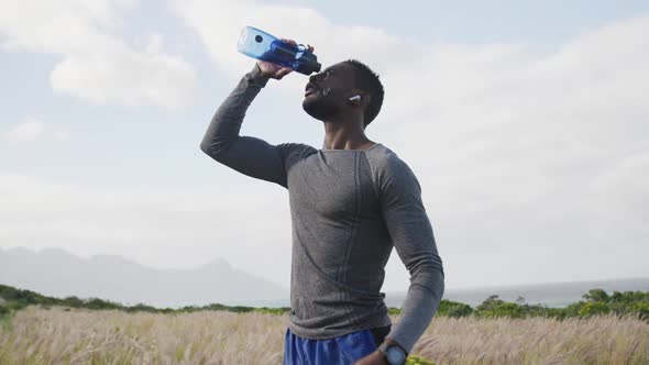 African american man pouring water on his face while exercising in countryside