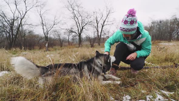 Young Beautiful Woman Walks and Plays with Her Husky Dog at Winter Around Forest