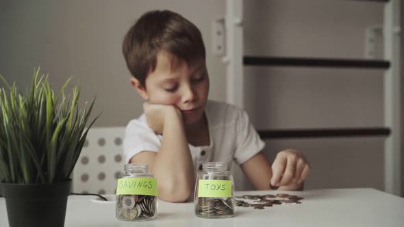 little caucasian boy putting coin into glass bottle at the table. Kid saving money for education