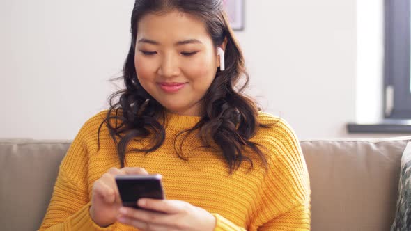 Asian Woman with Earphones and Smartphone at Home