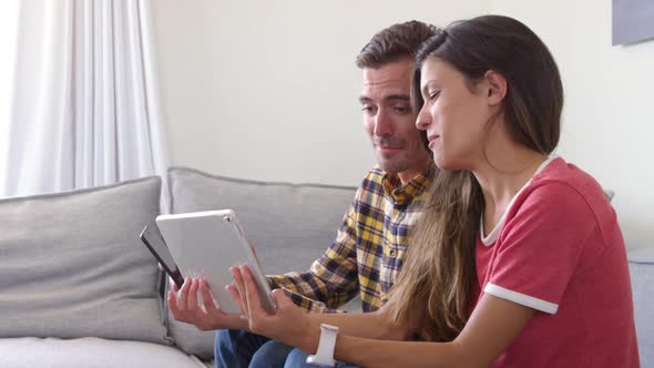 Young couple using mobile phone and digital tablet in living room at home 4k