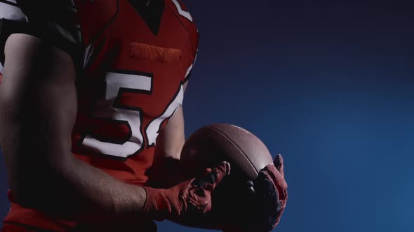 Faceless American Football Player Holding Ball Ready for Game and Attack on Blue Background