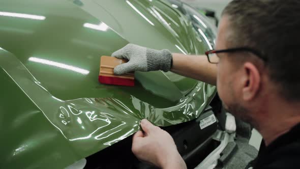 Two Men are Vinyl Wrapping a Car in Dark Green Color Using Plastic Cards