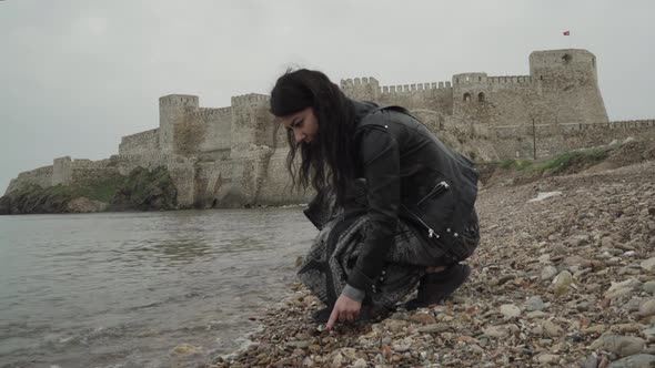 Young and beautiful girl collecting stones on the seaside in front of a castle.