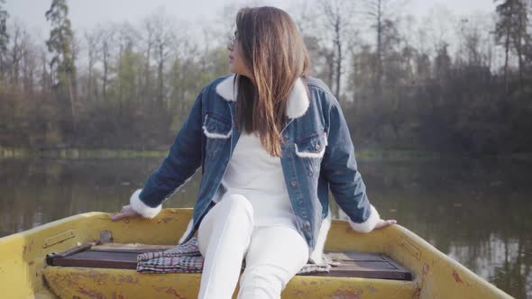 Portrait of a Charming Pretty Young Woman in Glasses and a Denim Jacket Floating on a Boat on a Lake