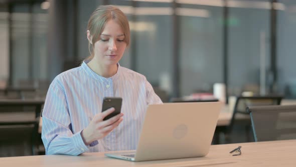 Young Woman Using Smartphone While Using Laptop in Office