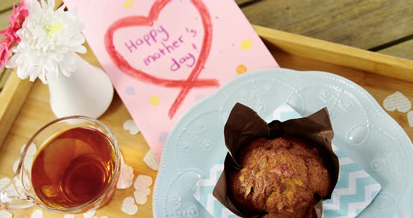 Cupcake, tea, flower vase and happy mothers day greetings card in tray