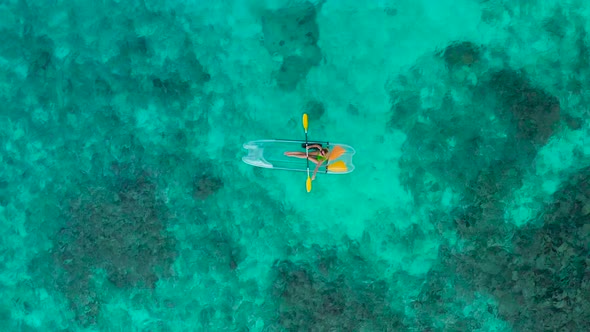 Aerial Top View of Beautiful Young Blonde Woman Kayaking the Floating Transparent Kayak on the