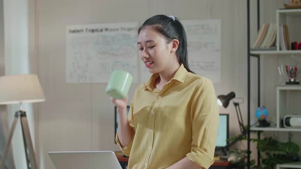 Asian Woman Engineer Sitting On The Table And Drinking Coffee While Using A Laptop To Work