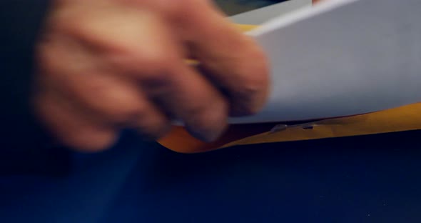 Close up on hands opening an orange envelope and placing important documents inside to be mailed and