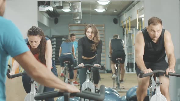 Back View of Trainer Instructing People on Cycling Equipment in Sports Club. Young Athletic Men and