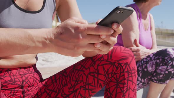 Caucasian women sitting down and woman using her phone on the beach and blue sky background