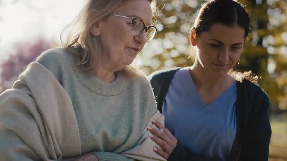 Young female nurse helping senior woman walking in park. Shot with RED helium camera in 8K