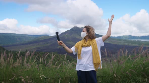 Female Travel Blogger in a Face Mask Recording Herself on a Camera in Mountains During Covid19