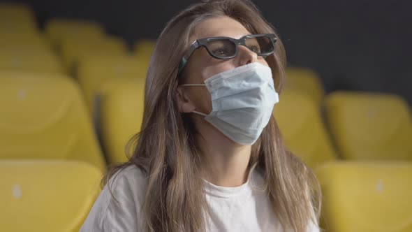 Close-up of Young Beautiful Brunette Woman in Face Mask Putting on 3d Glasses in Cinema. Portrait of