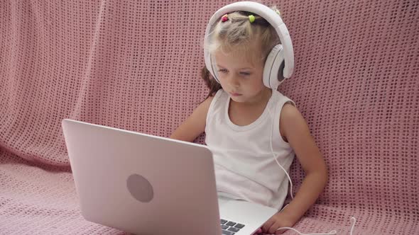 Little Girl Sitting Sofa in Headphones Listen Music Use Laptop Have Fun Home Interior Caucasian