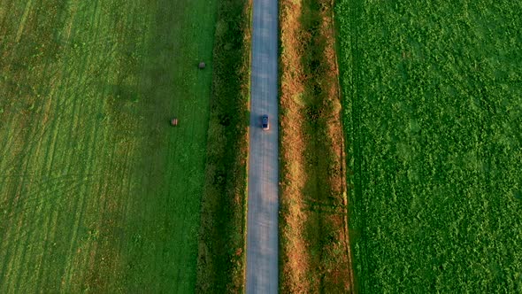 Top View of a Car Driving on the Road in a Field at Sunset in Summer