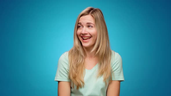 Young Pretty Woman Laughing and Gossiping Pointing Aside Against Blue Background