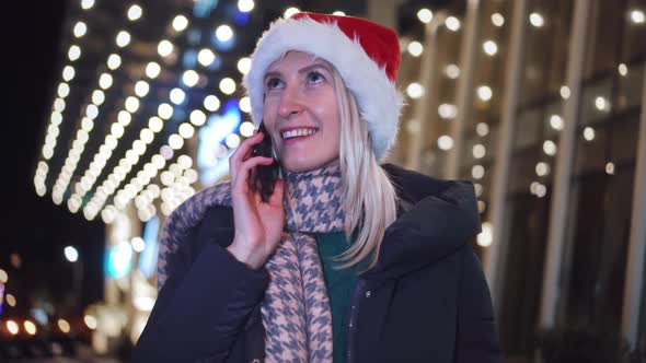 a woman chatting on her smartphone wearing a Santa hat is a night city.