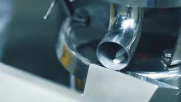 close up, locked off, shallow depth of field shot of white tablets exiting a gravity feed shoot in a