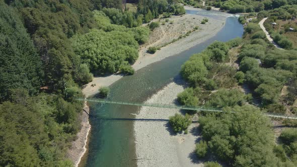 Arial high angle of Rio Azul river and enervated bridge between pine tree woods, Patagonia Argentina