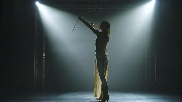 Silhouette of Dancing Greek Goddess Artemis with Bow and Arrow on Stage in a Dark Studio with Smoke