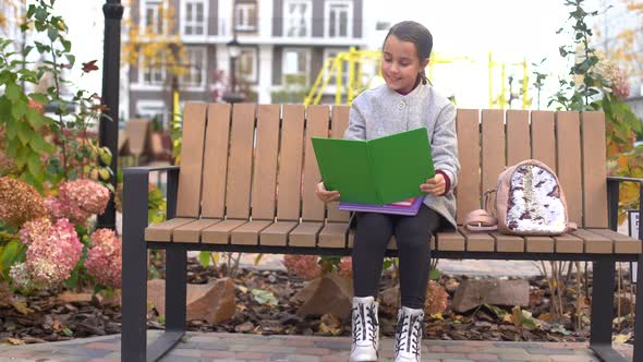 Schoolgirl Reading Book While Sitting on Bench in Park