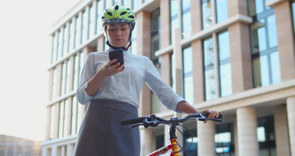 Attractive Businesswoman Using Cell Phone Near Office Holding Bike