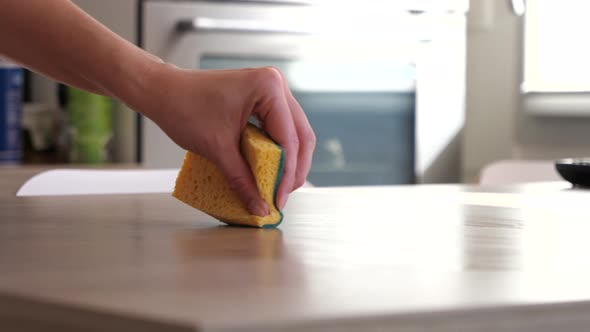 Woman cleaning the kitchen table with a yellow sponge.