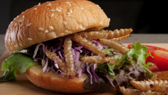 Burger with fried bamboo caterpillar and vegetable salad on wooden plate.