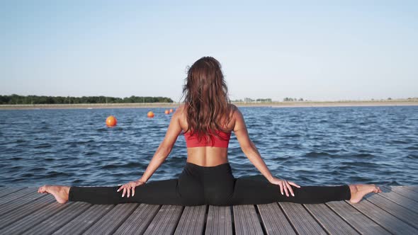 athletic girl sits in split against lake Engaged in stretching Flexibility
