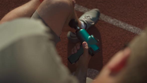 An Athlete Massages with a Percussion Therapy Gun to Relieve the Pain of Muscle Aches After a