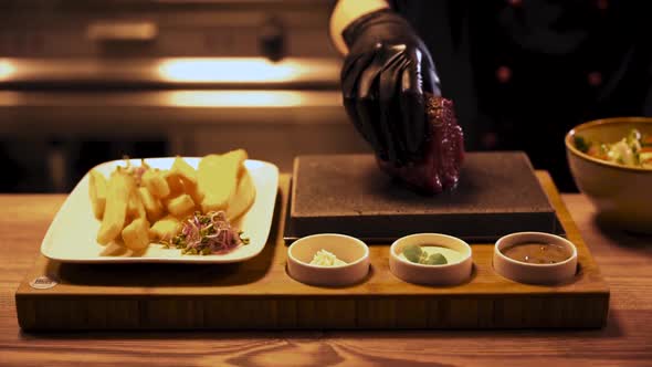 Cook preparing raw piece of meat on hot cooking stone, cinematic shot