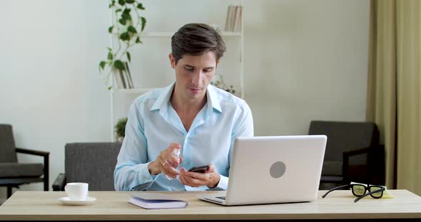 Young Caucasian Businessman Sitting at His Desk at Home or in Office, He Uses Sanitizer