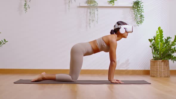 Asian woman using VR goggles practicing yoga cat cow workout in Metaverse online community.Yoga trai