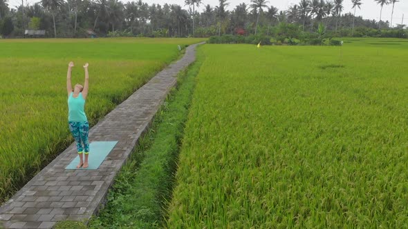 Aerial Slowmotion Shot of a Young Woman Practicing Yoga on a Beautiful Rice Field