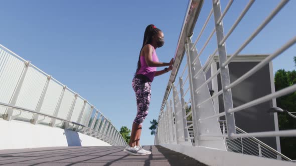 African american woman stretching her leg holding the railing of the city bridge