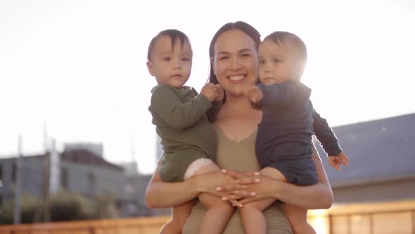 Happy Asian Mom Posing with Twin Babies Outdoors in Sun