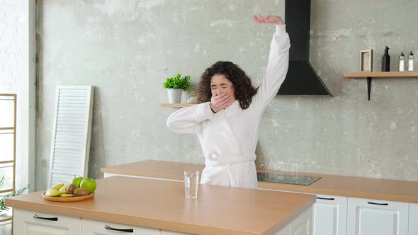 Happy Sleepy Woman Stretching and Drinks a Glass of Water in Early Morning