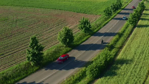 Motorcyclist Rides on Road Aprroaching Cars Aerial View