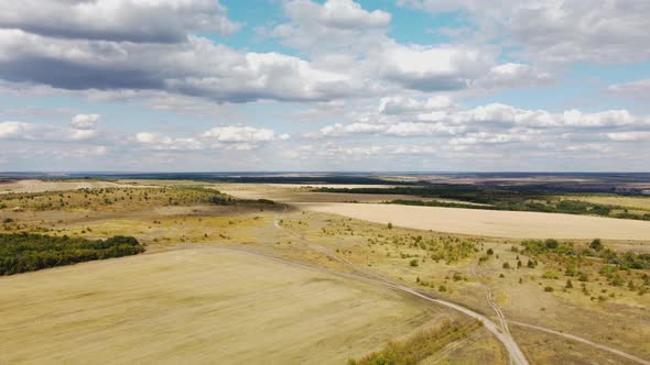 a Dirt Road Among Autumn Fields and a Blue Sky with Clouds From a Height