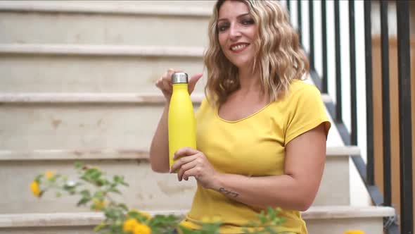 Close up of women in yellow t-shirt, opening yellow reusable steel bottle