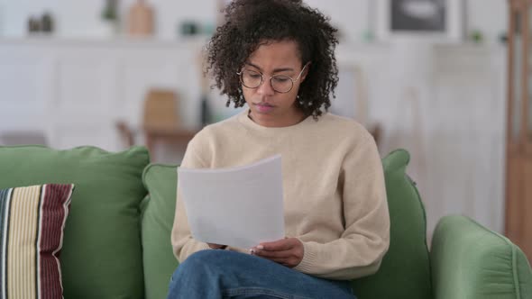 Young African Woman Reading Documents on Sofa 