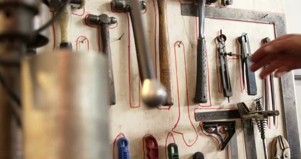 Welder taking hammer from tool rack