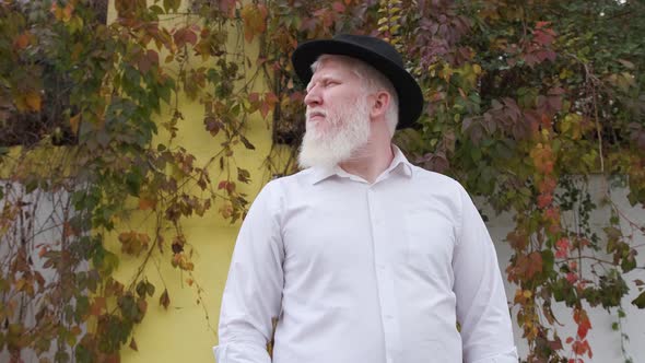 Older Man with Albinism in White Shirt and Hat Near His House