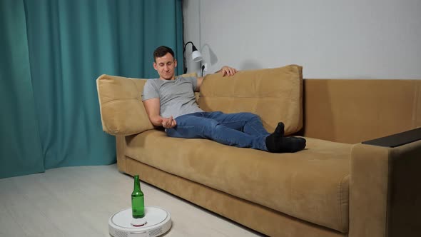Robot Vacuum Cleaner Delivers Alcohol to Man Sitting on Sofa