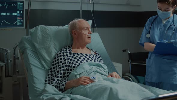 Nurse Checking File of Sick Patient Laying in Hospital Ward