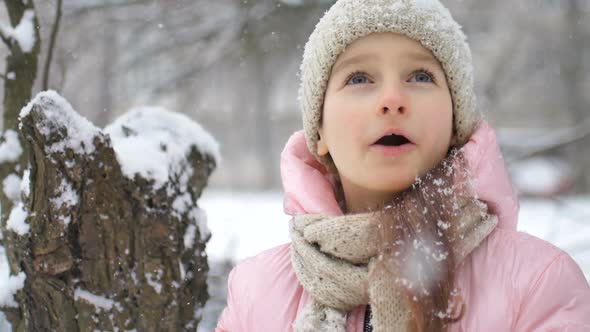 Winter Portrait of a Kid Girl in Pink Coat Wearing Beige Hat and Mittens Playing Outdoor in Snowy